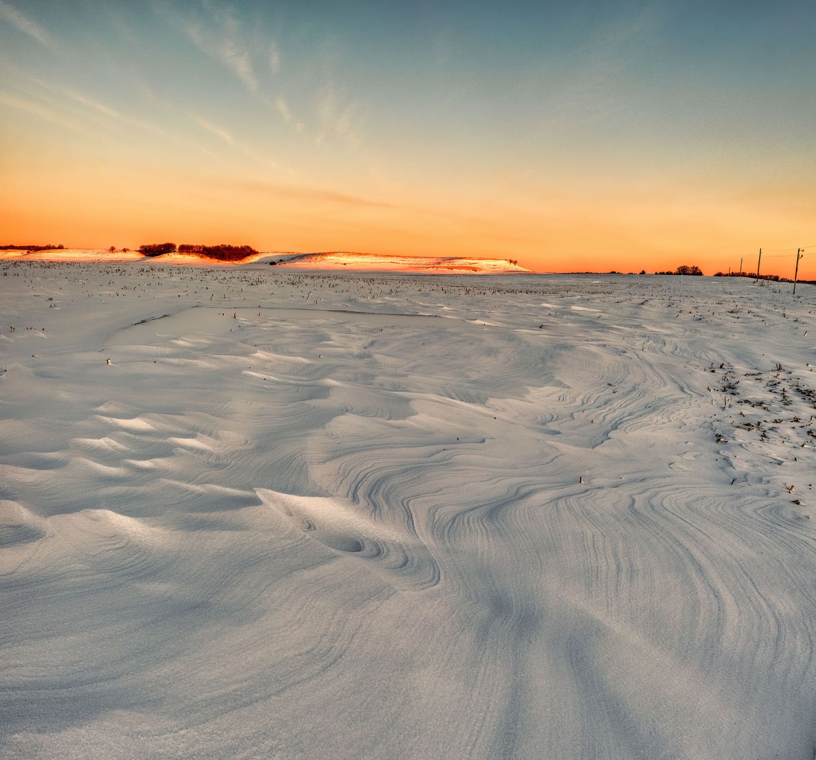 Snow carved into drifts by the wind across a wide, open field — the blowing snow that snow removal Gloucester routes have to come back for