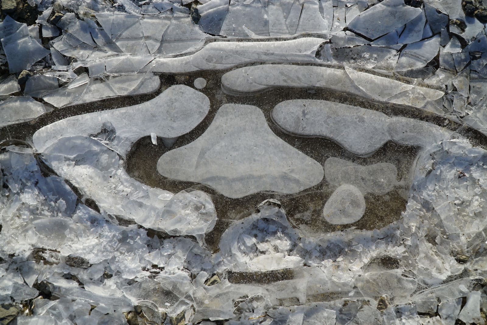 De l’eau de fonte regelée en une plaque de glace craquelée sur du gravier — ce que devient une entrée en pente tassée, et ce que le déneigement Westboro dégage avant que cela se forme